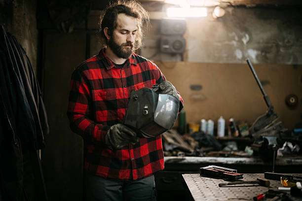 Man holding a welding helmet in a workshop.