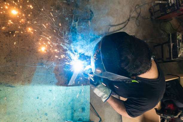 Overhead view of a person wearing a welding helmet while actively welding with bright sparks.