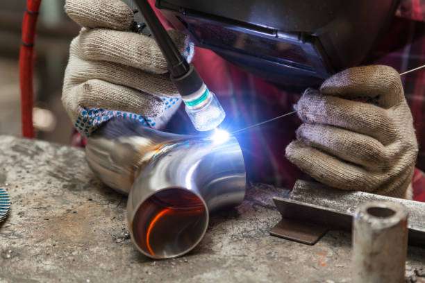 Close-up of a welder wearing a Welding Helmet, actively joining metal pipe with bright arc.